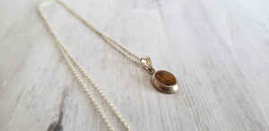 Vintage small oval tiger eye sterling silver  pendant on 18" 925 silver chain, Gray Barn Eclectic Finds online vintage store, flat on table, shows side stepped profile of pendant