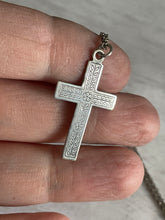 Load image into Gallery viewer, cross up of mid century antique sterling silver cross, so the flower and leaf pattern is more visible, held against a bare hand