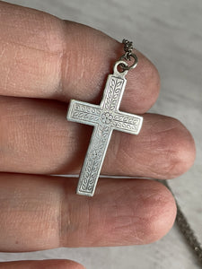 a second close up of the antique silver cross being held in a hand to show the pattern