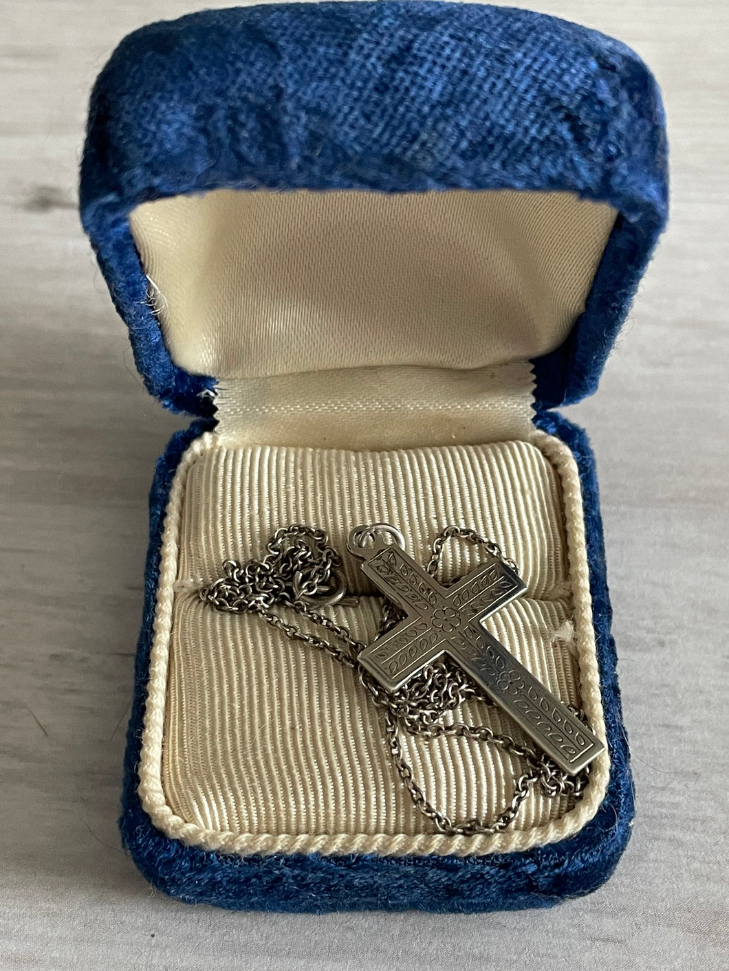 antique silver cross with chain, featuring an embossed flower and leaf design, places in an antique blue velvet ring box